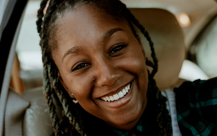 A smiling commuter with a work lanyard in the back seat of a car